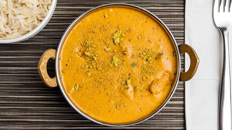 Overhead view of a copper karahi filled with creamy orange curry, served with white rice.